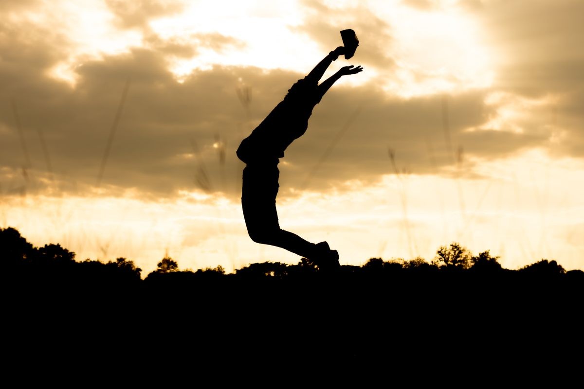 Silhouette man jumps with arms raised with energy for victory. success outdoors concept.